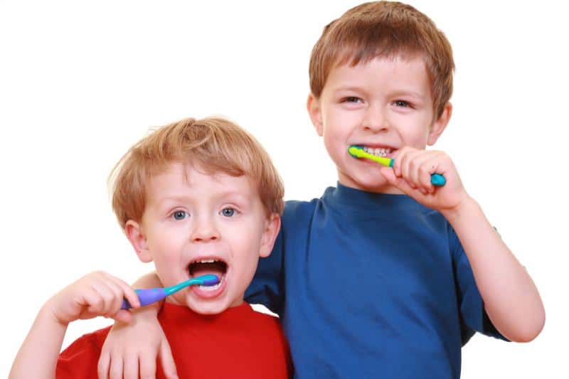 Two young boys looking at the camera while brushing their teeth