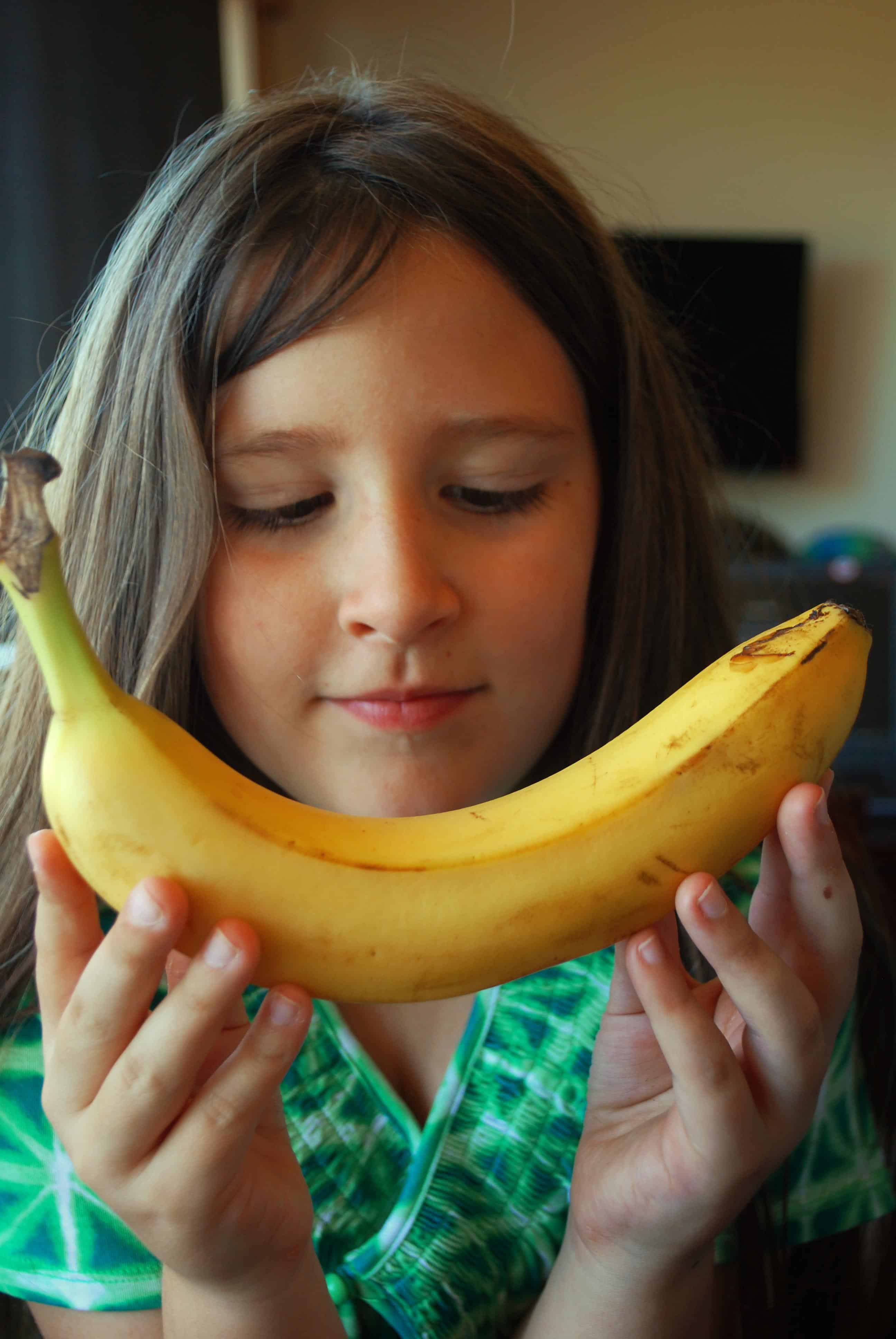 Young girl staring down at a yellow banana in her hands