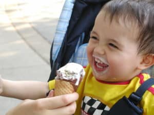 Young child laughing at the camera while eating an ice cream cone