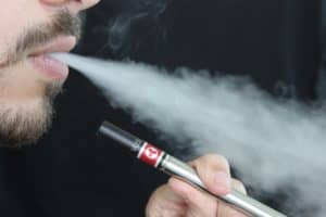 Close-up of man's mouth blowing out vapor from e-cigarette